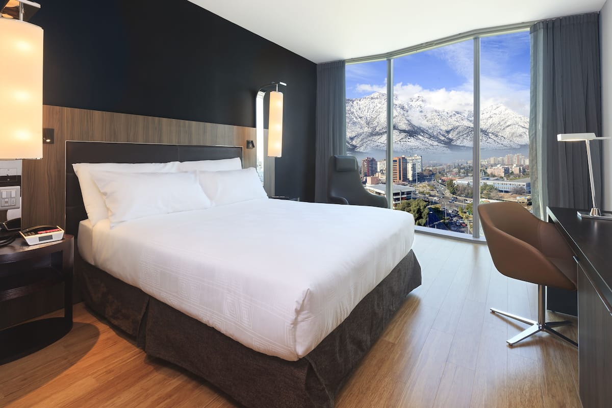 A hotel room with a large bed, a desk, and a view of a city and mountains.