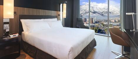 A hotel room with a large bed, a desk, and a view of a city and mountains.