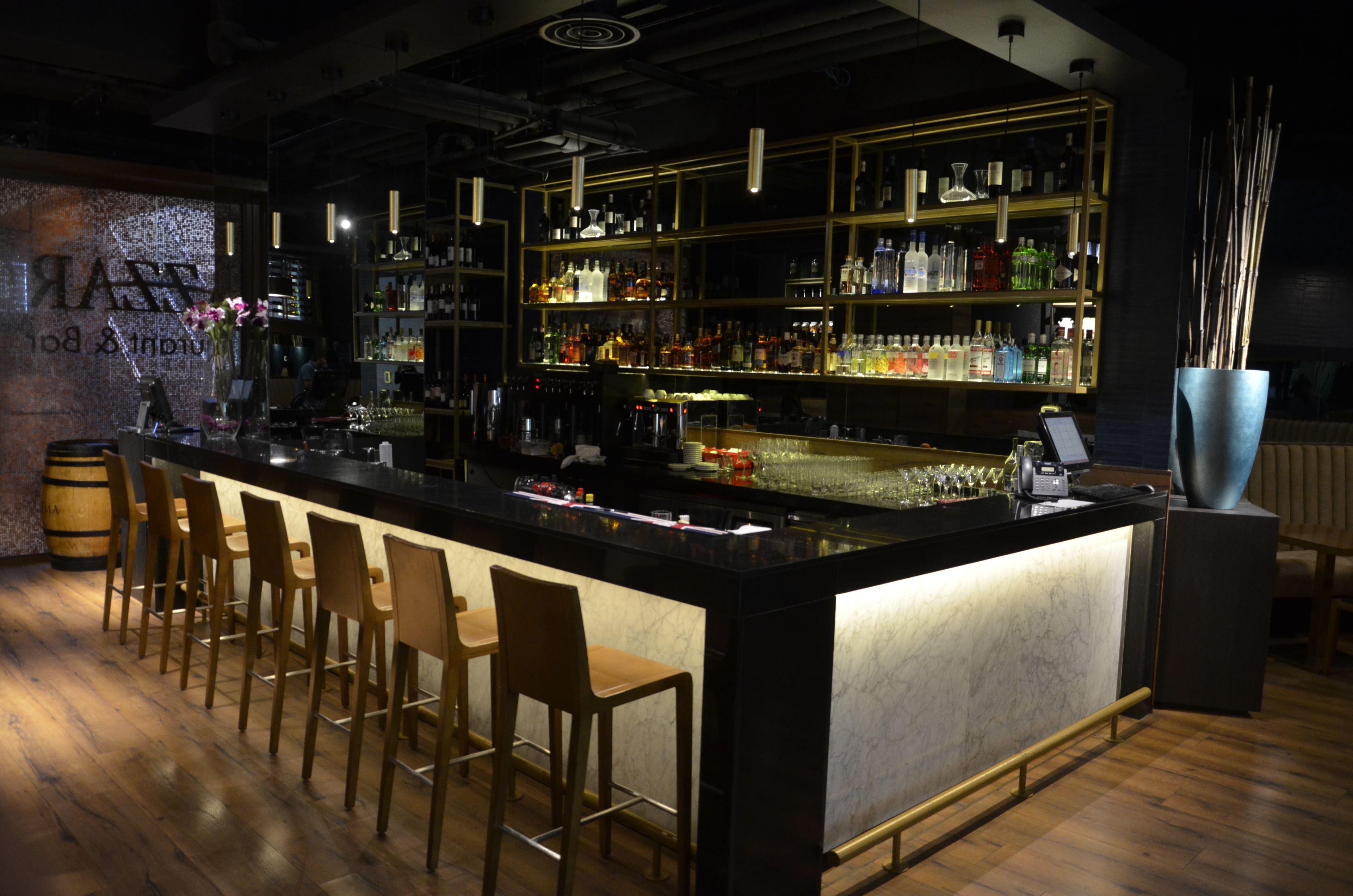Un espace bar doté d’un comptoir en marbre, de chaises en bois et d’étagères remplies de bouteilles.