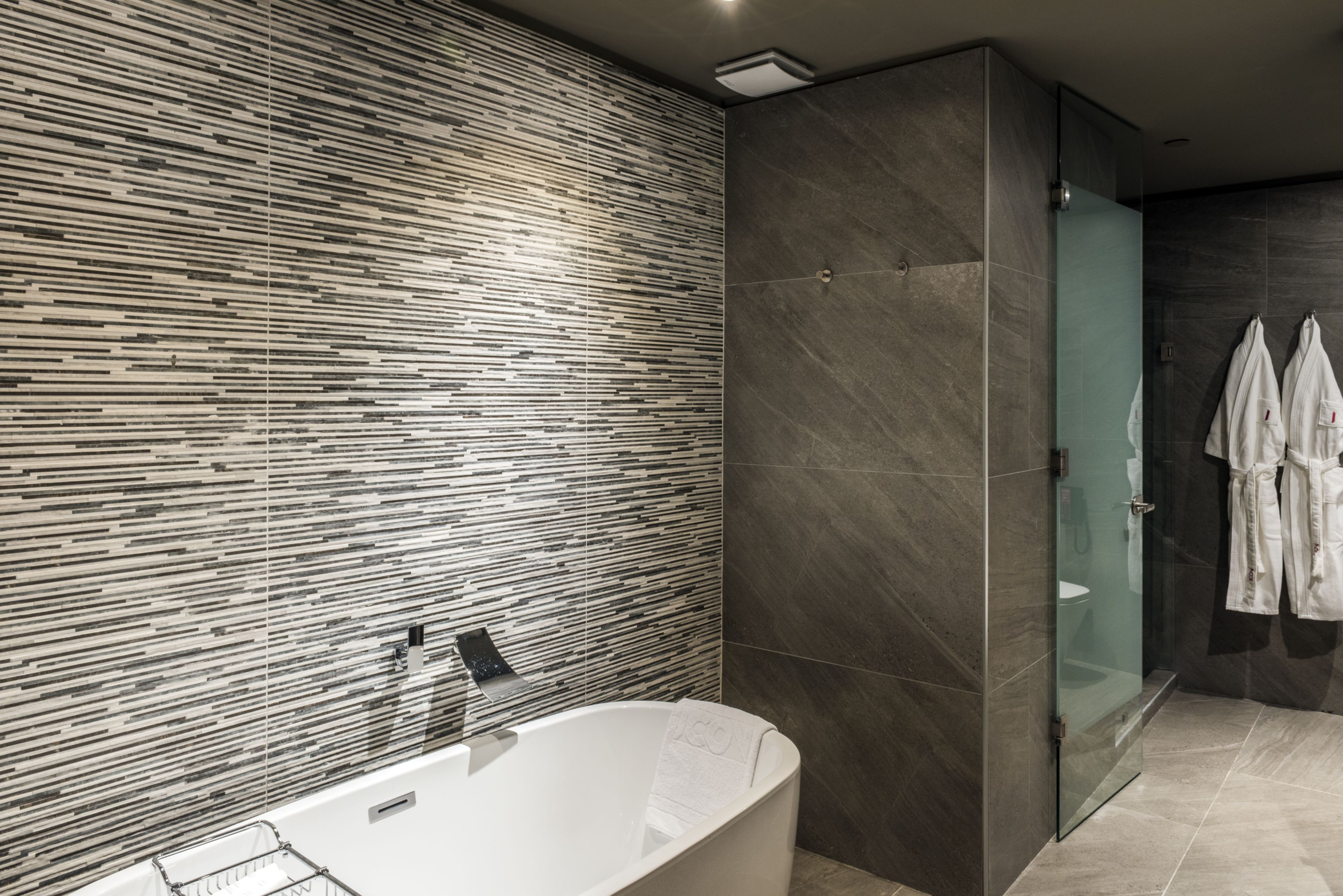 A modern bathroom with a freestanding bathtub, a glass shower enclosure, and a tiled wall with a linear pattern.