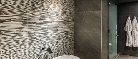 A modern bathroom with a freestanding bathtub, a glass shower enclosure, and a tiled wall with a linear pattern.
