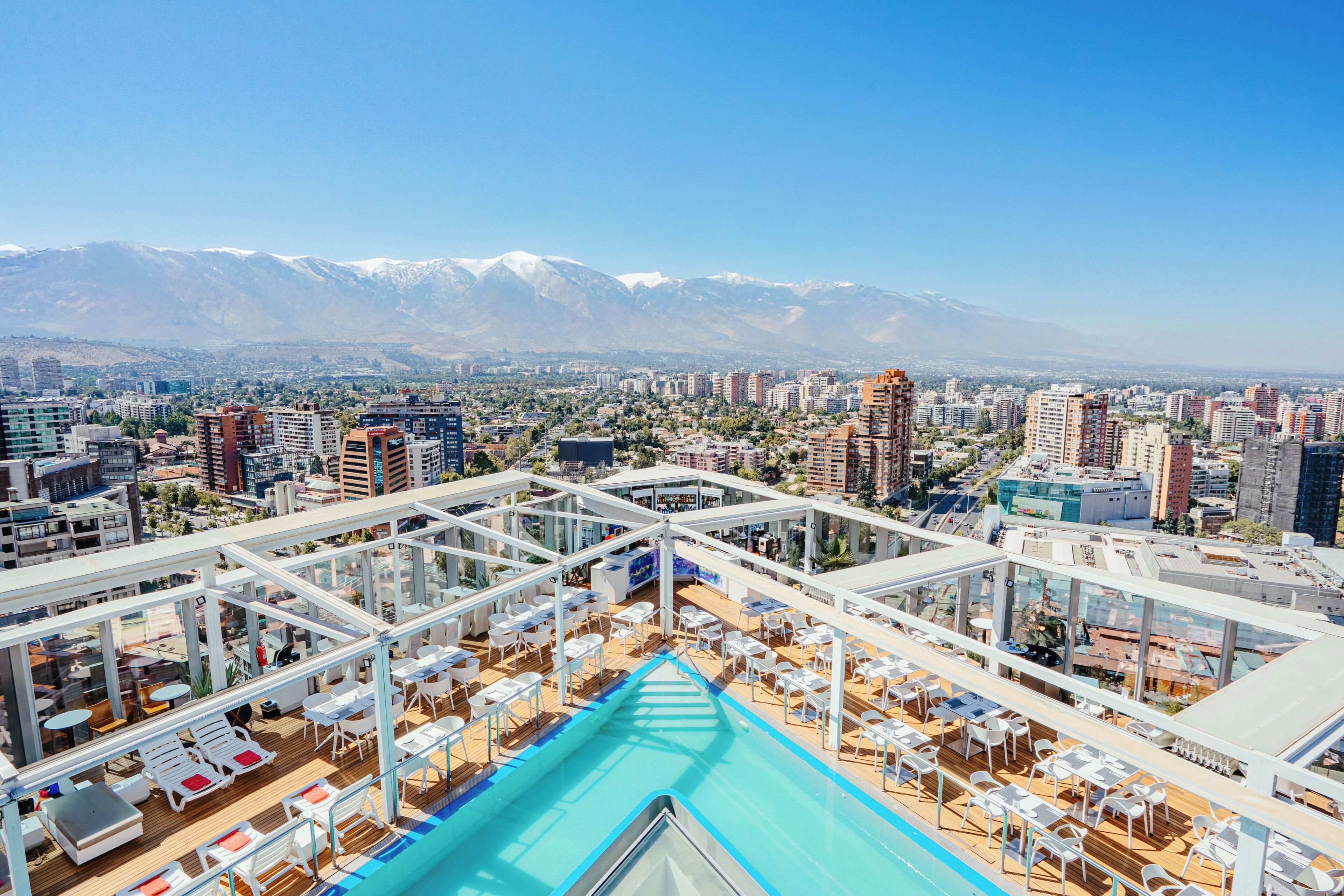 Un área de piscina en la azotea con vista a un paisaje urbano y montañas al fondo.
