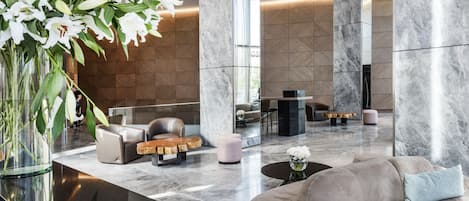 A spacious lobby with a marble floor, leather sofas, a coffee table, and a large vase of white flowers.