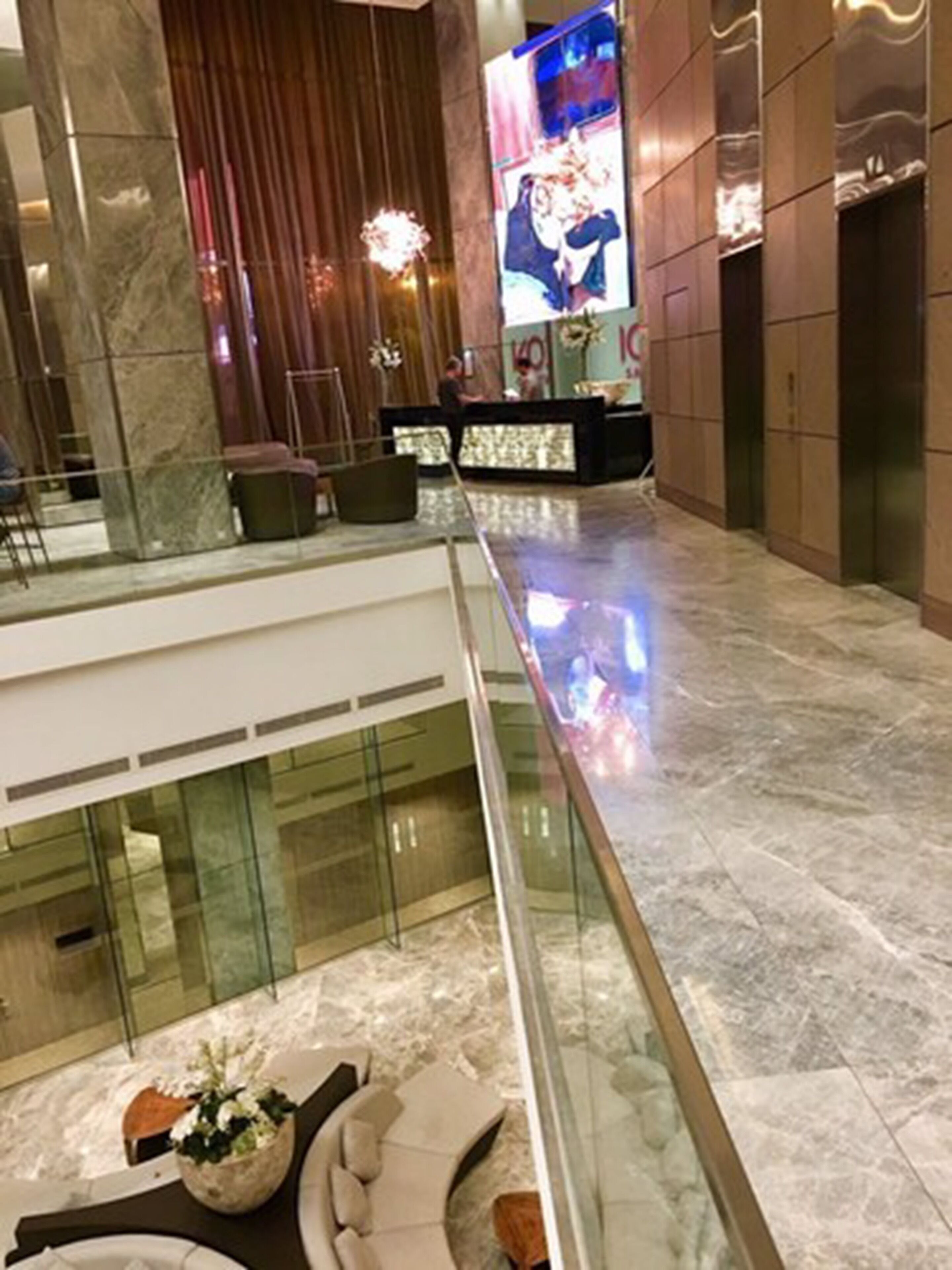 Un vestíbulo moderno con piso de mármol, barandilla de vidrio y una zona de estar con una planta.