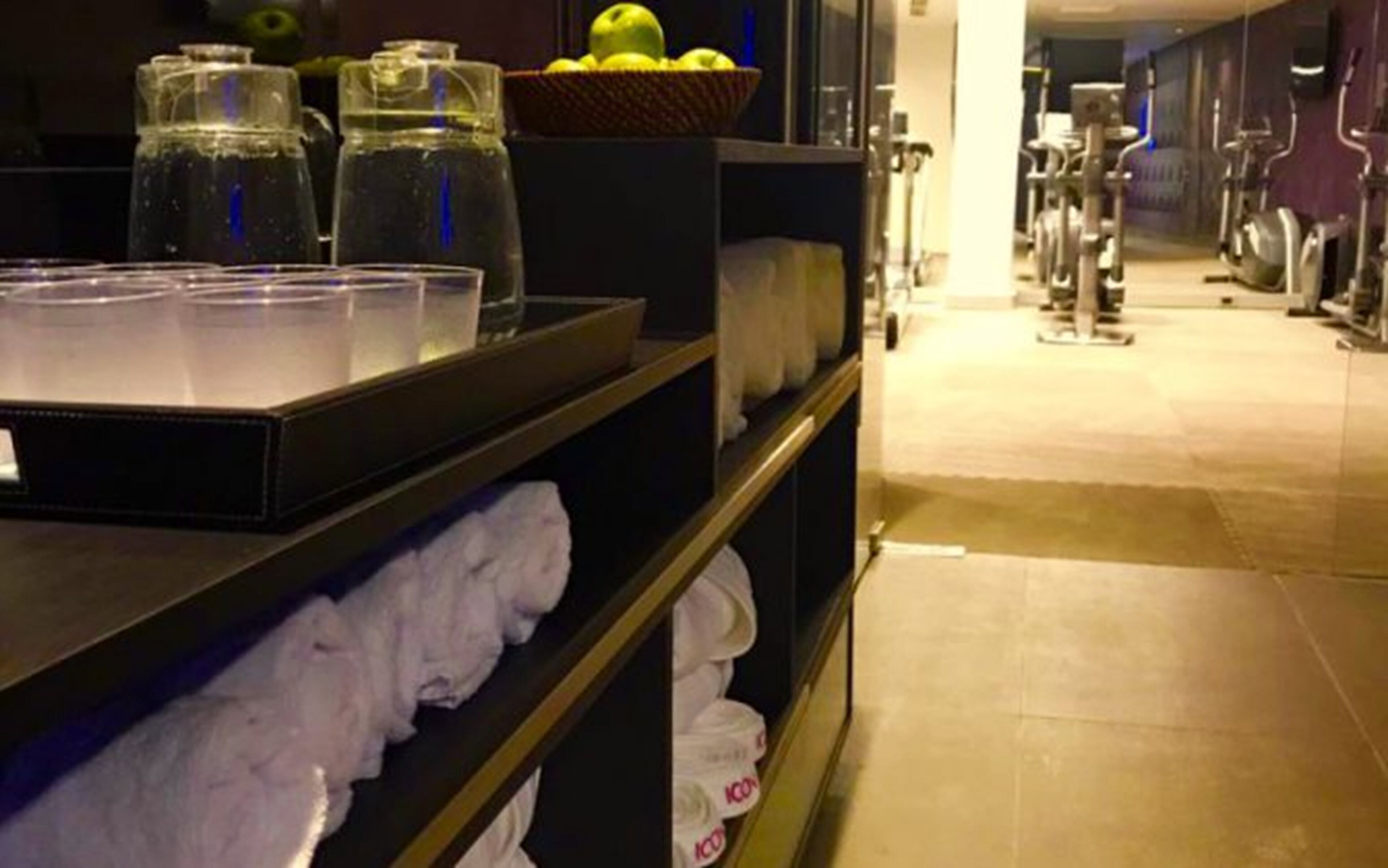 A hotel room with a shelf containing towels, a basket of fruit, and water bottles.