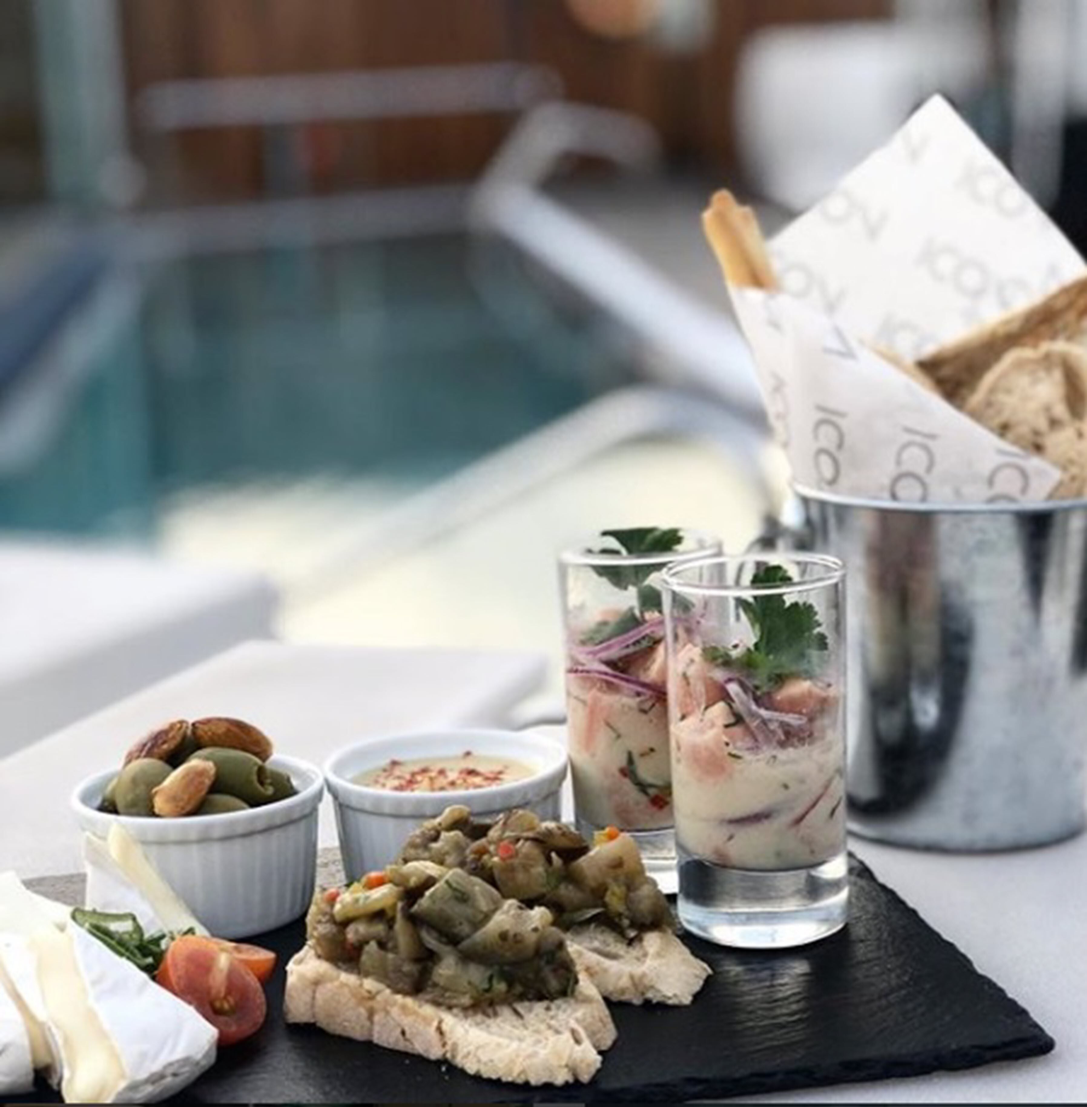 Tavola da pranzo con vista sulla piscina, con un piatto di cibo, due bicchieri di una bevanda cremosa e ciotole piccole di frutta secca e spezie.