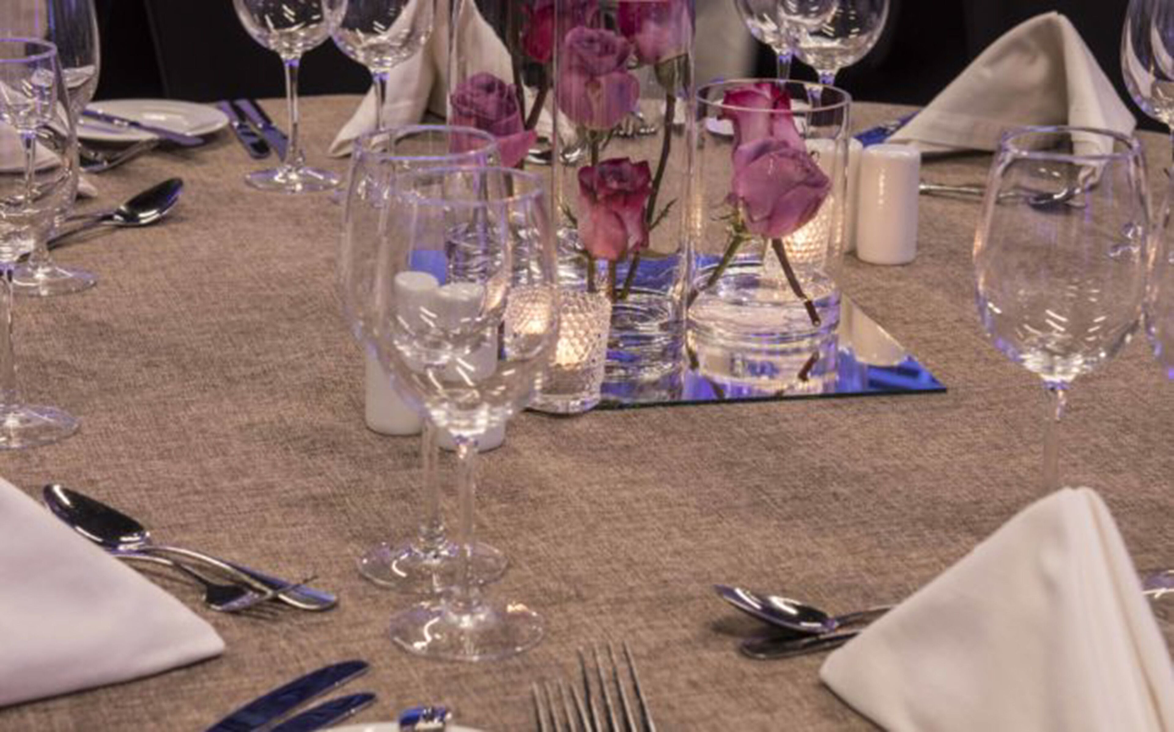 A table set for a formal dinner with wine glasses, cutlery, and a centerpiece of purple flowers.