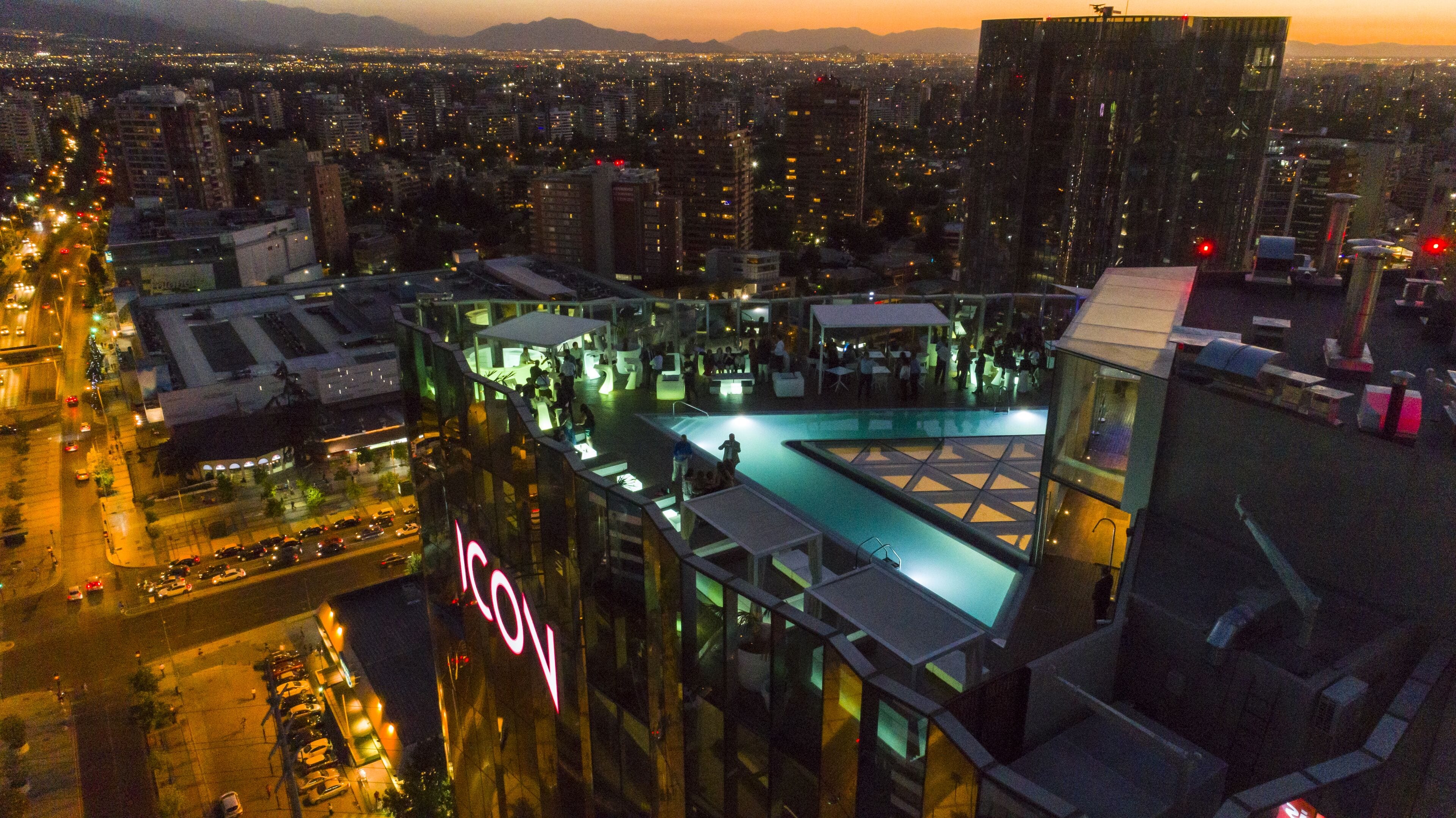 A high-rise hotel with a rooftop pool and a view of the cityscape at dusk.