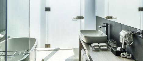 Un baño moderno con ducha envuelta en vidrio, una bañera independiente, un tocador de madera con espejo y un perchero para toallas.