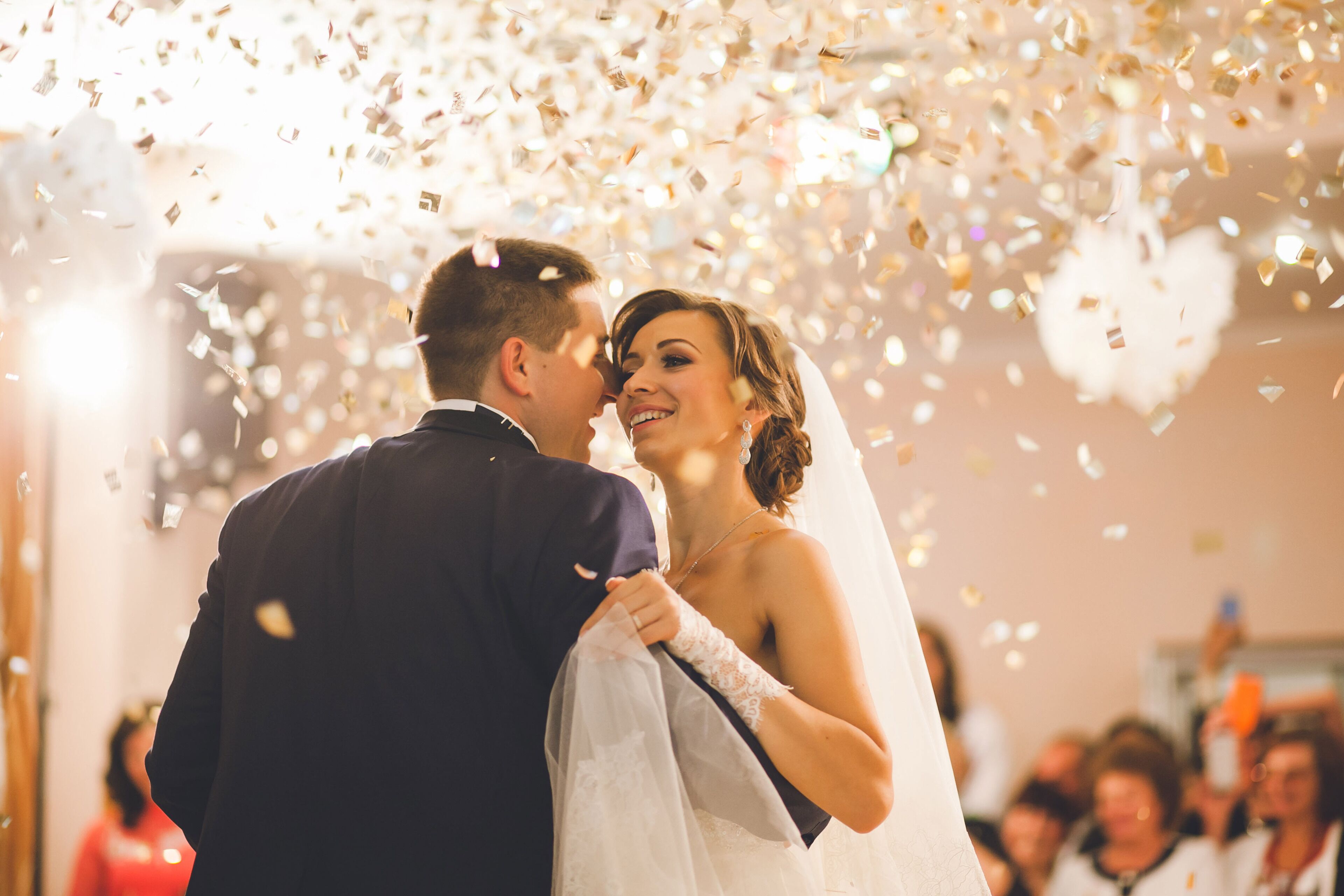 A couple embracing at a wedding reception with confetti falling around them.