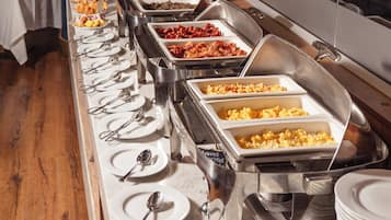 A buffet setup with various food items in metal containers, arranged on a long table with plates and cutlery.
