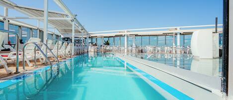 Zona de piscina con sillones reclinables y bar en la cubierta de un crucero.