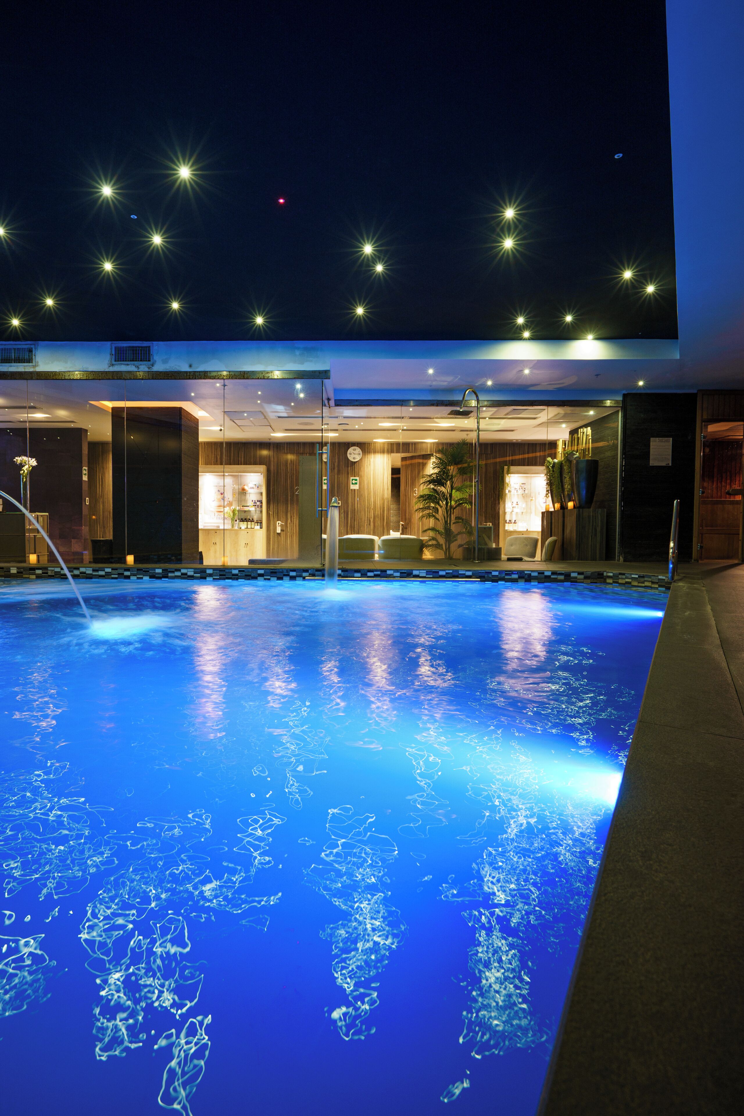 A swimming pool with a clear blue water surface, surrounded by a building with a modern design, featuring a reception area and a bar.