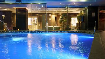 A swimming pool with a clear blue water surface, surrounded by a building with a modern design, featuring a reception area and a bar.
