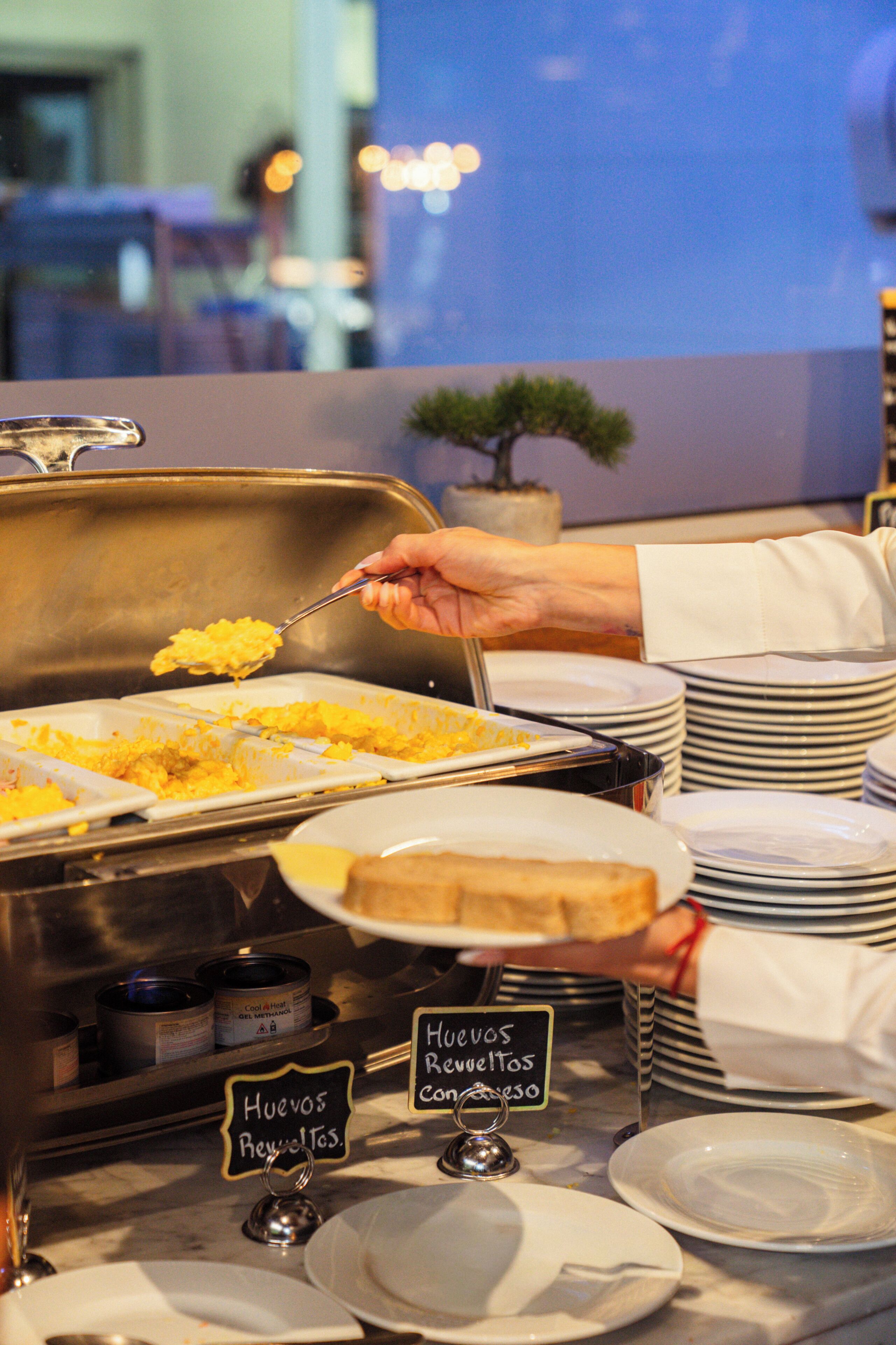 A buffet setup with labeled dishes and a sign indicating 'Huevos Rellenos Con Salsa'.