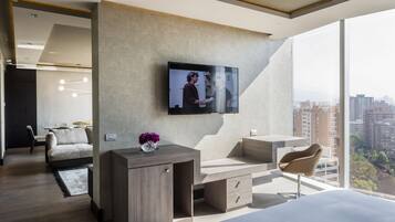 Quarto de hotel moderno com uma cama grande, uma escrivaninha, uma cadeira, uma TV na parede e vista para a cidade.