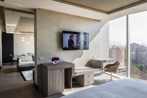 Quarto de hotel moderno com uma cama grande, uma escrivaninha, uma cadeira, uma TV na parede e vista para a cidade.