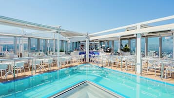 Un área de piscina en la azotea con asientos y un bar, con vistas al paisaje urbano.