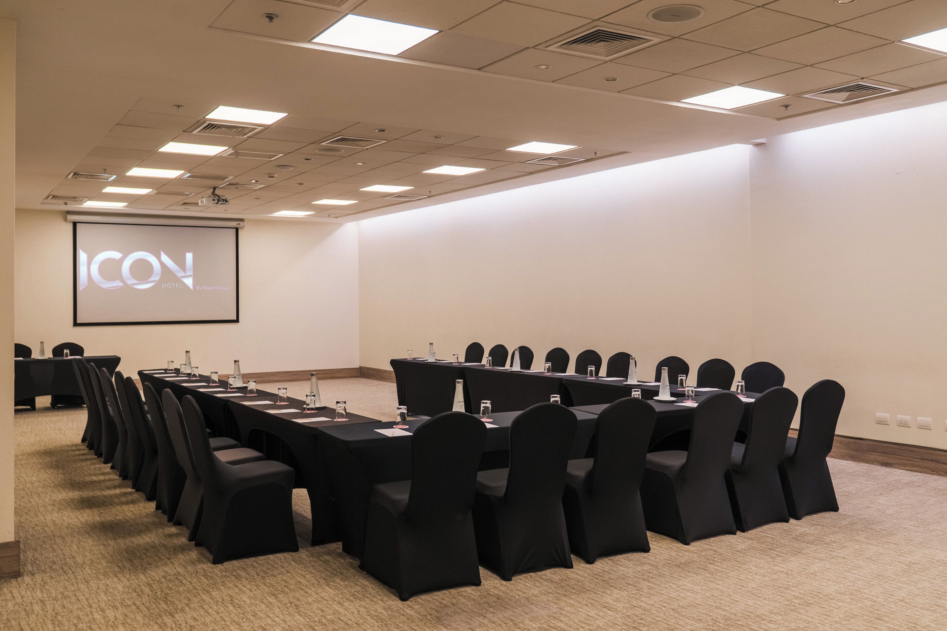 Une salle de conférence avec une longue table, des chaises et un écran de projection affichant le mot « ICON ».