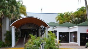 Un edificio con un vestíbulo cubierto, una estatua en el centro y un jardín circular con plantas.