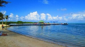A beach with a pier extending into the water, a covered seating area, and a clear blue sky. - Hotel Decameron Marazul (San Andres)