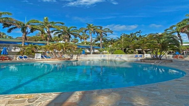 A swimming pool with palm trees, lounge chairs, and a clear blue sky. - Hotel Decameron Marazul (San Andres)