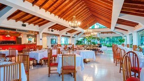 A spacious dining area with wooden ceiling beams, tables set for dining, and large windows offering views of greenery. - Hotel Decameron Marazul (San Andres)
