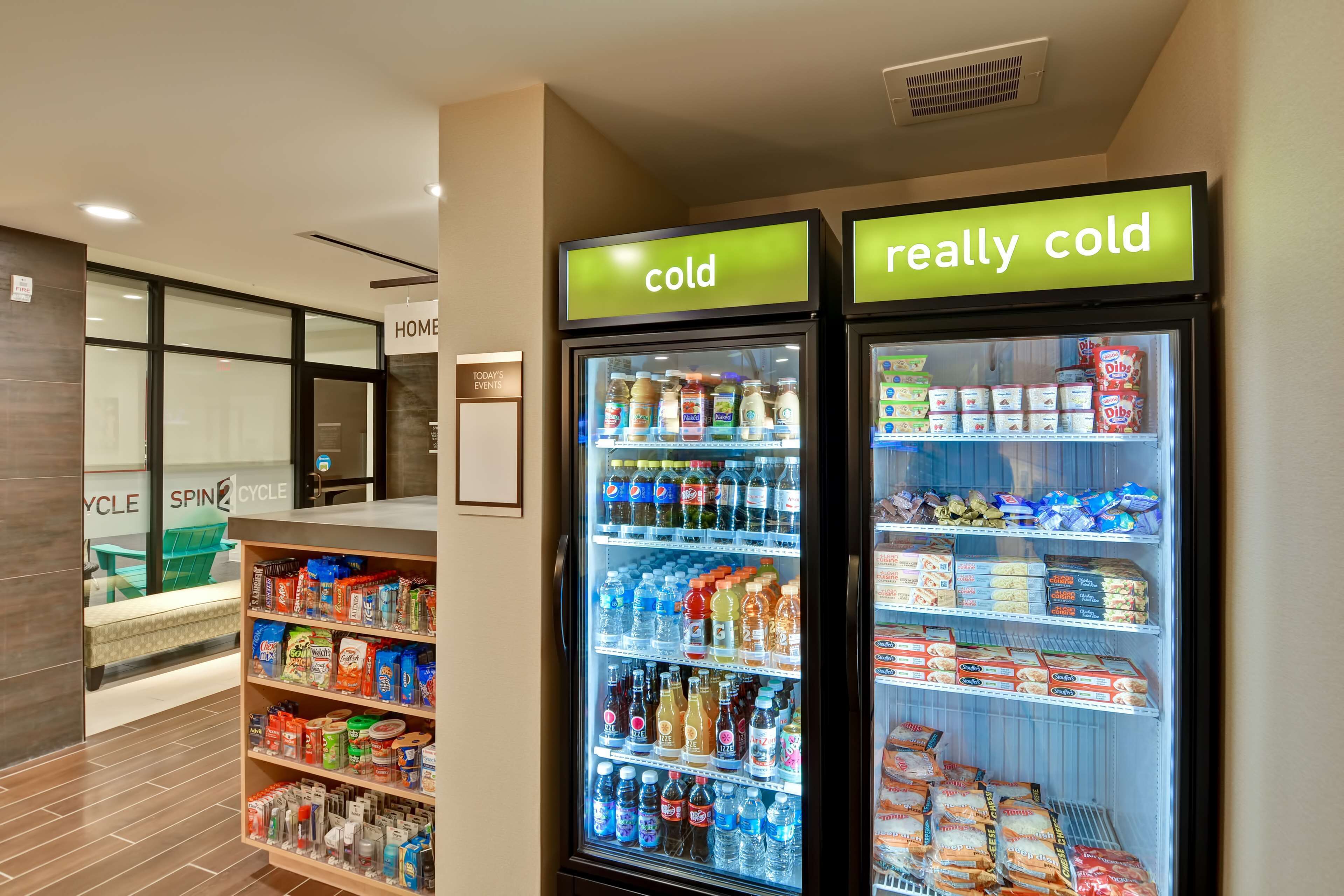 A hotel lobby with a cold and really cold beverage refrigerator, a reception desk, and a seating area with a green chair.