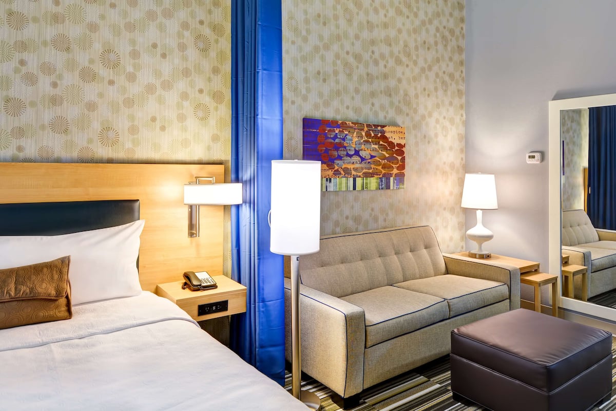 Une chambre d’hôtel avec un lit, un canapé, une petite table, une lampe et un miroir.