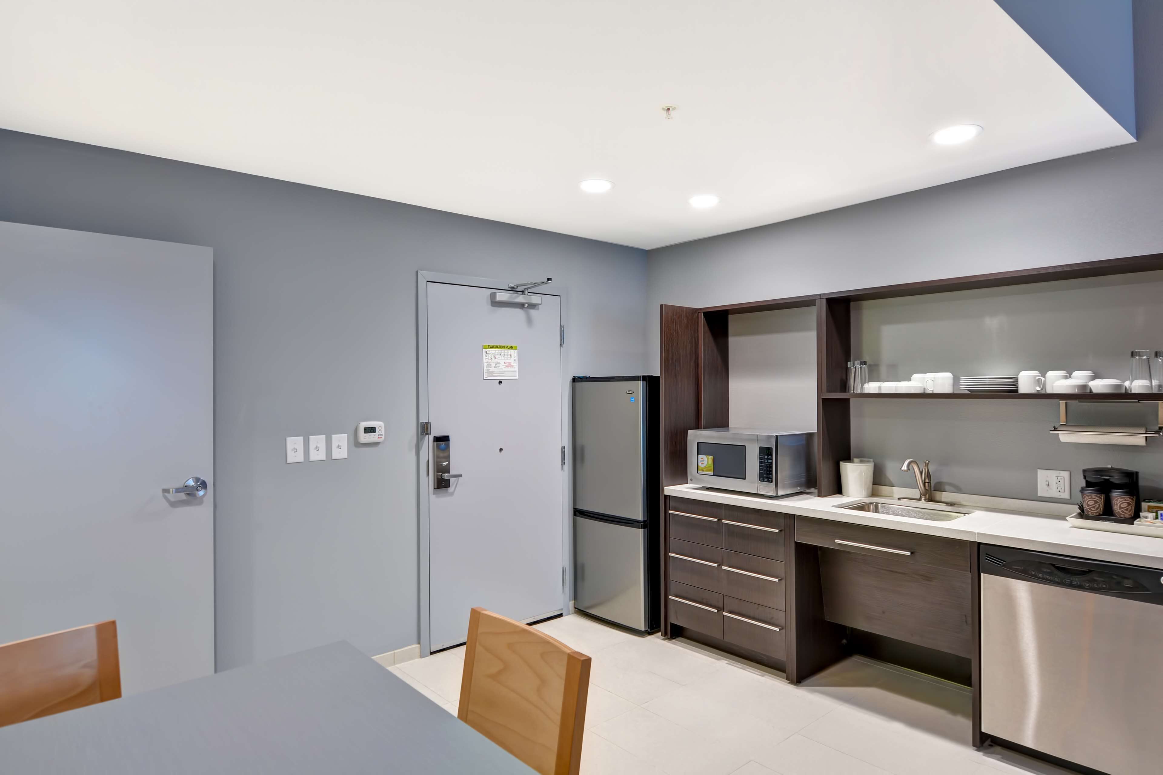 A modern kitchen with a built-in microwave, refrigerator, and dishwasher. There is a dining table with chairs and a cabinet with glass doors above it.
