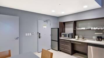 Una cocina moderna con microondas integrado, refrigerador y lavavajillas. Hay una mesa de comedor con sillas y un armario con puertas de vidrio arriba.