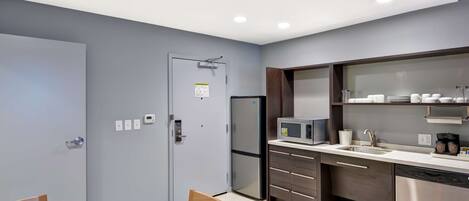 A modern kitchen with a built-in microwave, refrigerator, and dishwasher. There is a dining table with chairs and a cabinet with glass doors above it.