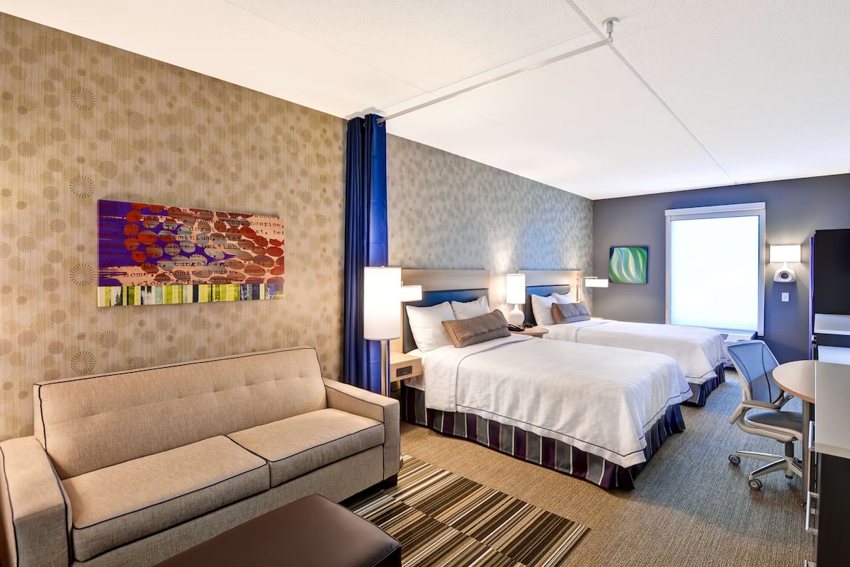 Une chambre d’hôtel avec un canapé, deux lits, un bureau et une grande fenêtre.