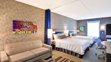 Una habitación de hotel con sofá, dos camas, un escritorio y un ventanal grande.