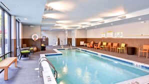 An indoor swimming pool with clear water, surrounded by chairs and a bench. - Home2 Suites by Hilton Stafford Quantico (Stafford)