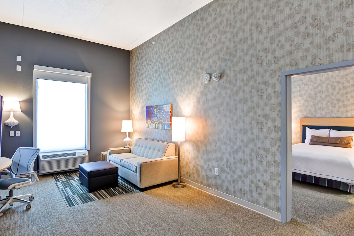 Une chambre d’hôtel avec un canapé, un bureau, une chaise, une table de chevet, une lampe, un tableau et un lit.