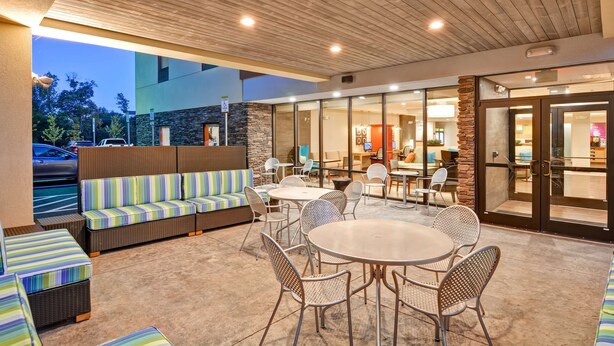 An outdoor patio area with seating and tables, stone accents, and a view of the street. - Home2 Suites by Hilton Stafford Quantico (Stafford)