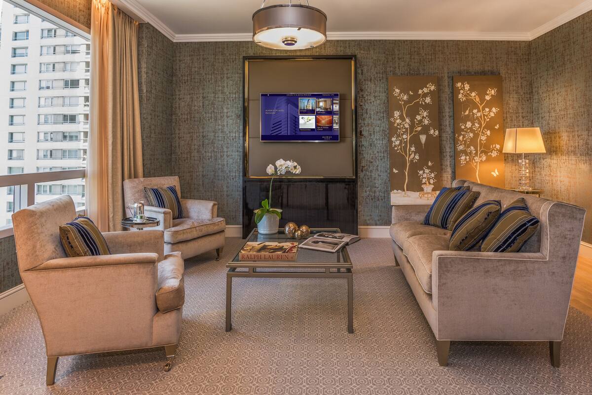Un salon comprenant un canapé, un fauteuil et une table basse, un téléviseur à écran plat fixé au mur et une plante décorative.