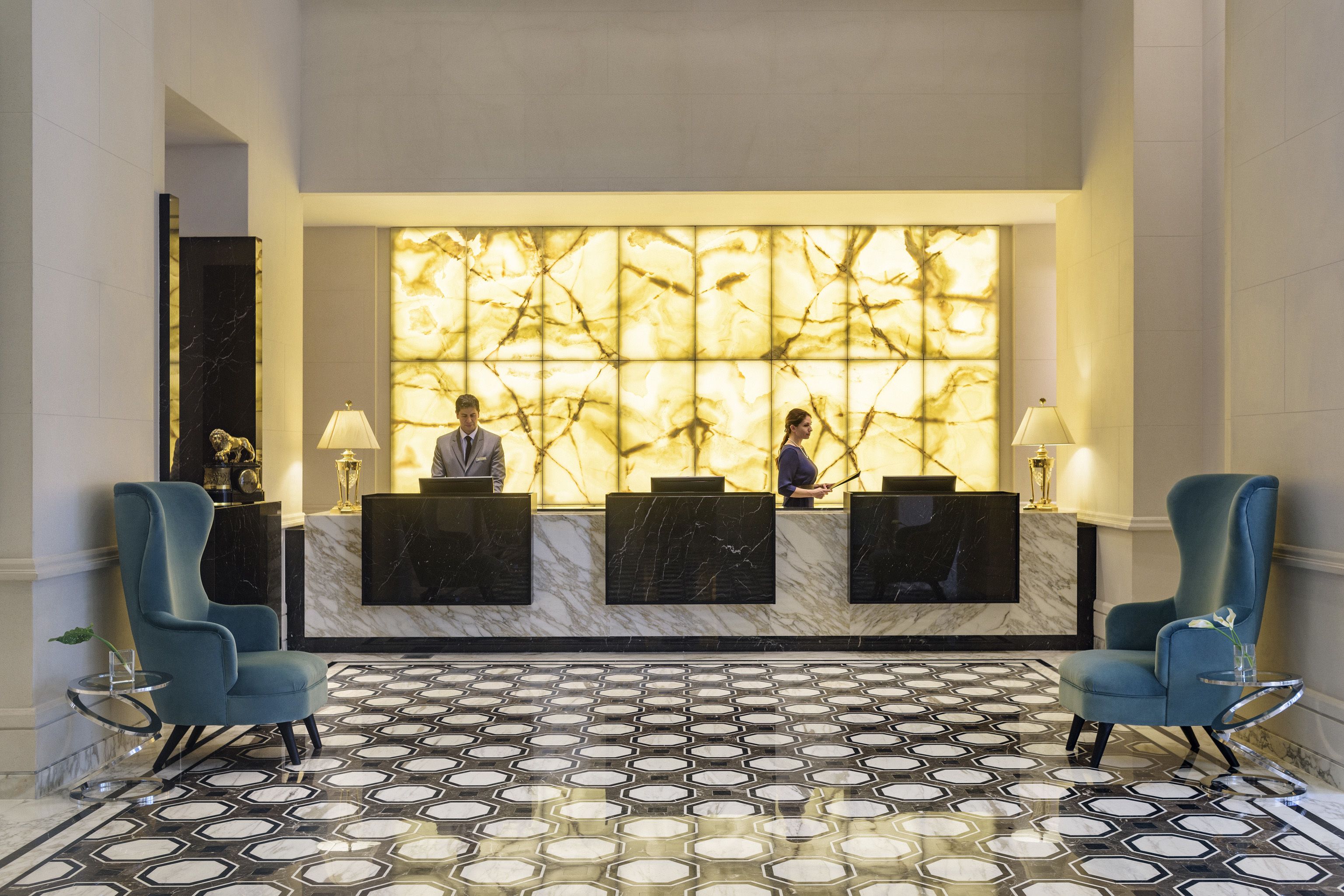 A reception area with a marble reception desk, two blue chairs, and a patterned floor.