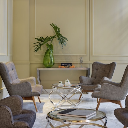 A modern living room with four grey upholstered armchairs, a glass coffee table, and a green plant on a console table.