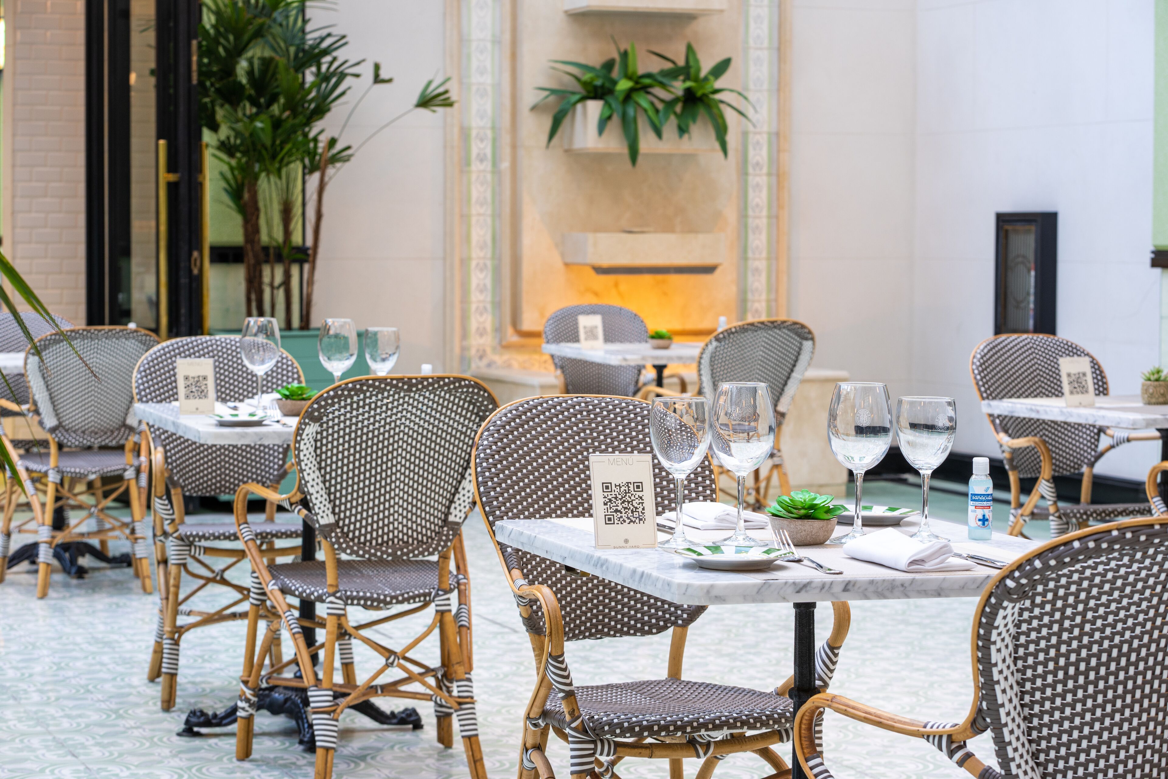 A dining area with wicker chairs and tables, QR codes on the tables, and potted plants.