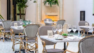 A dining area with wicker chairs and tables, QR codes on the tables, and potted plants.