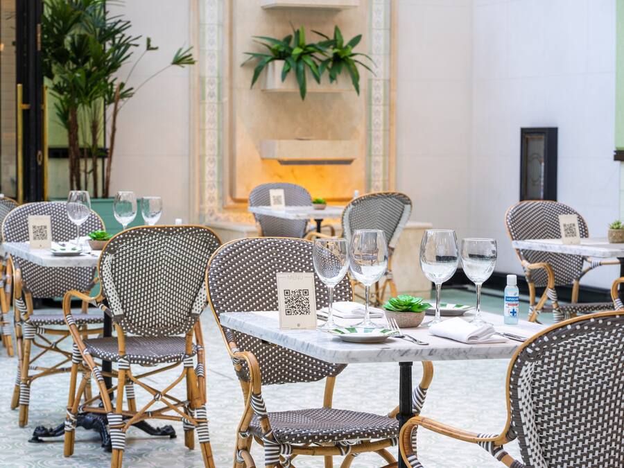 A dining area with wicker chairs and tables, QR codes on the tables, and potted plants.