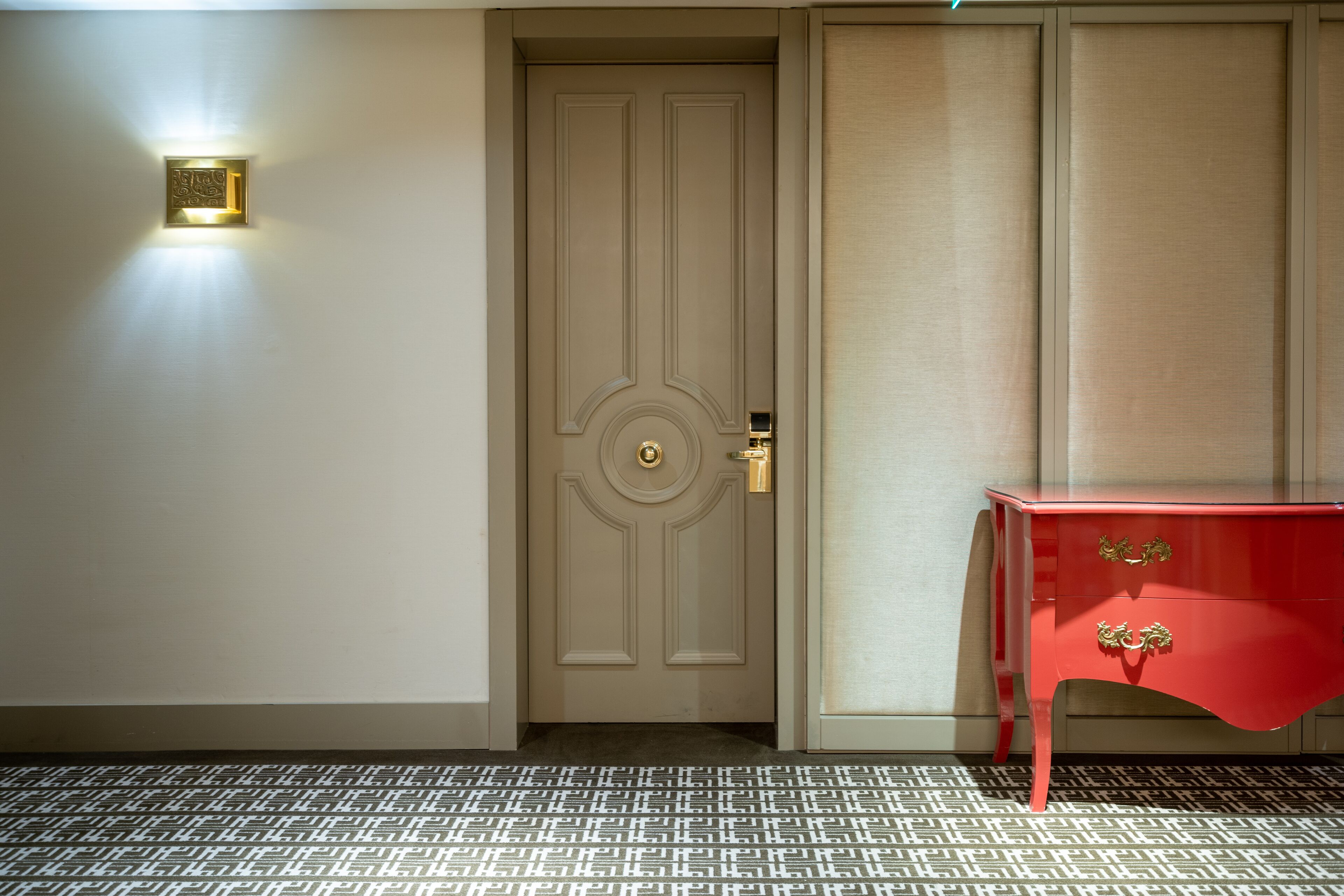 A door with a light fixture above it and a red table with gold handles.