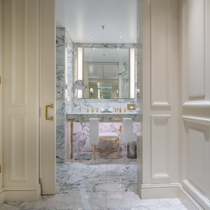 A luxurious bathroom with marble floors, a large mirror, and a gold-framed vanity.