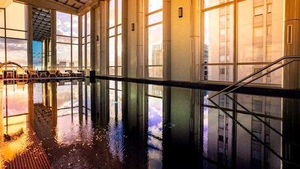 A spacious indoor swimming pool with clear reflections on the water, large windows, and a modern architectural design.