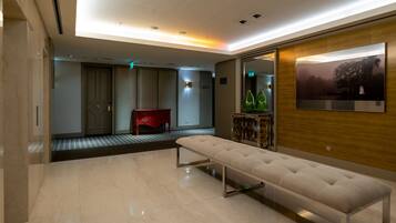 A modern hotel lobby with a marble floor, a bench, a red chair, and a wall-mounted TV.