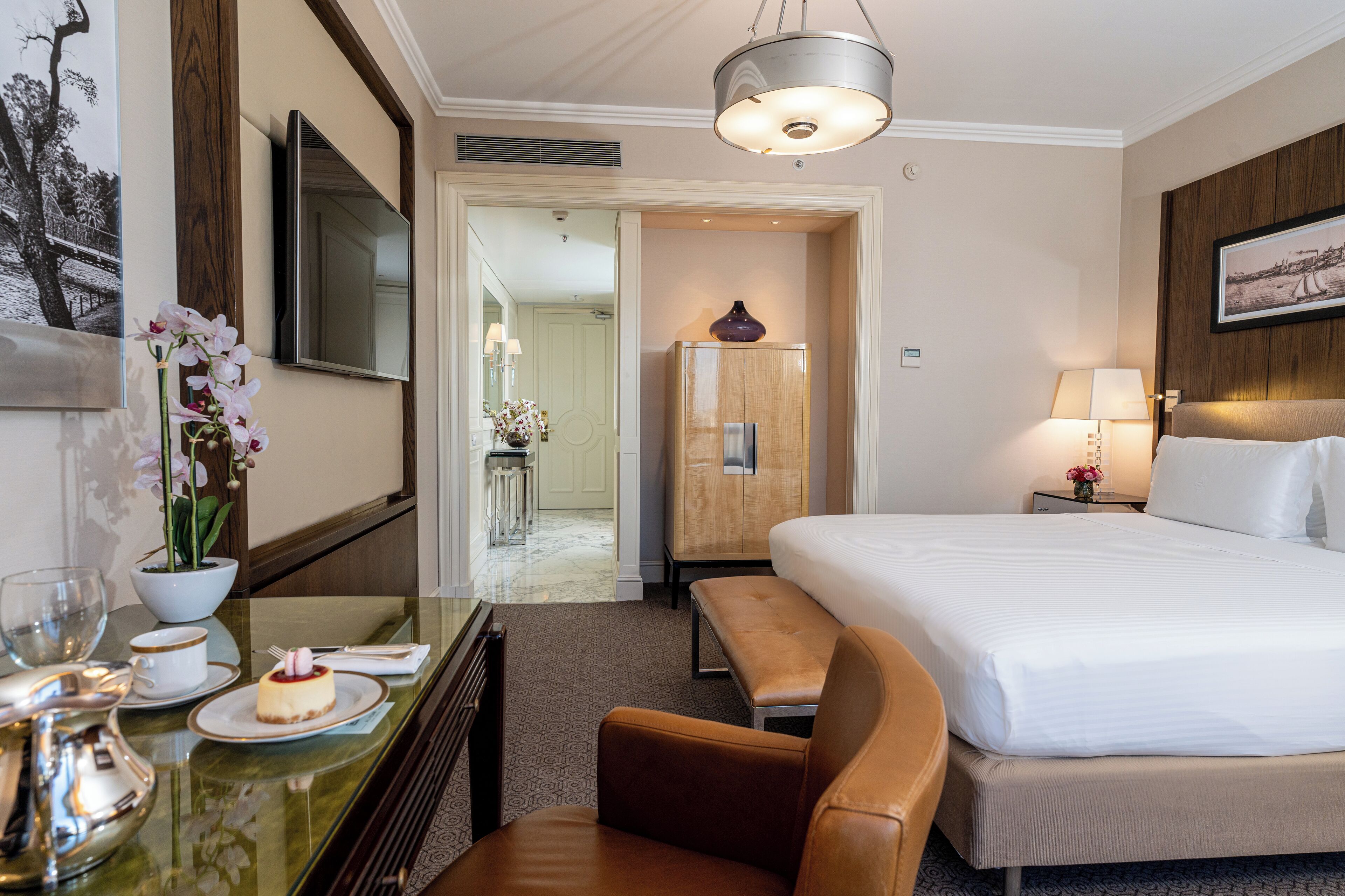 A hotel room with a bed, a desk with a vase of flowers, a lamp, and a television.