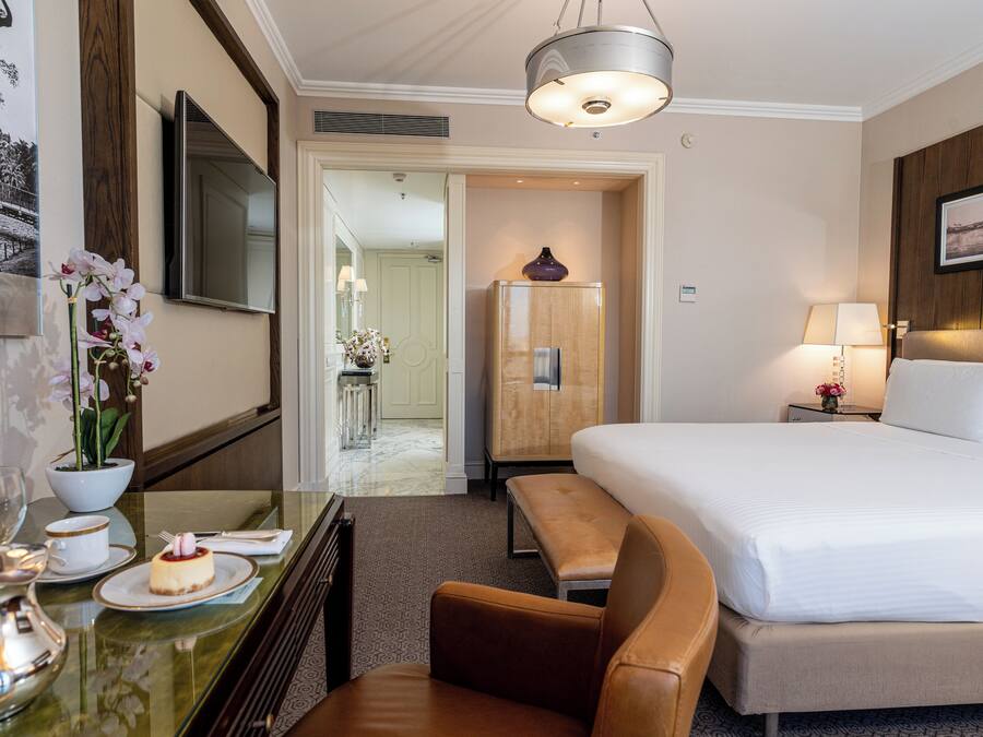 A hotel room with a bed, a desk with a vase of flowers, a lamp, and a television.