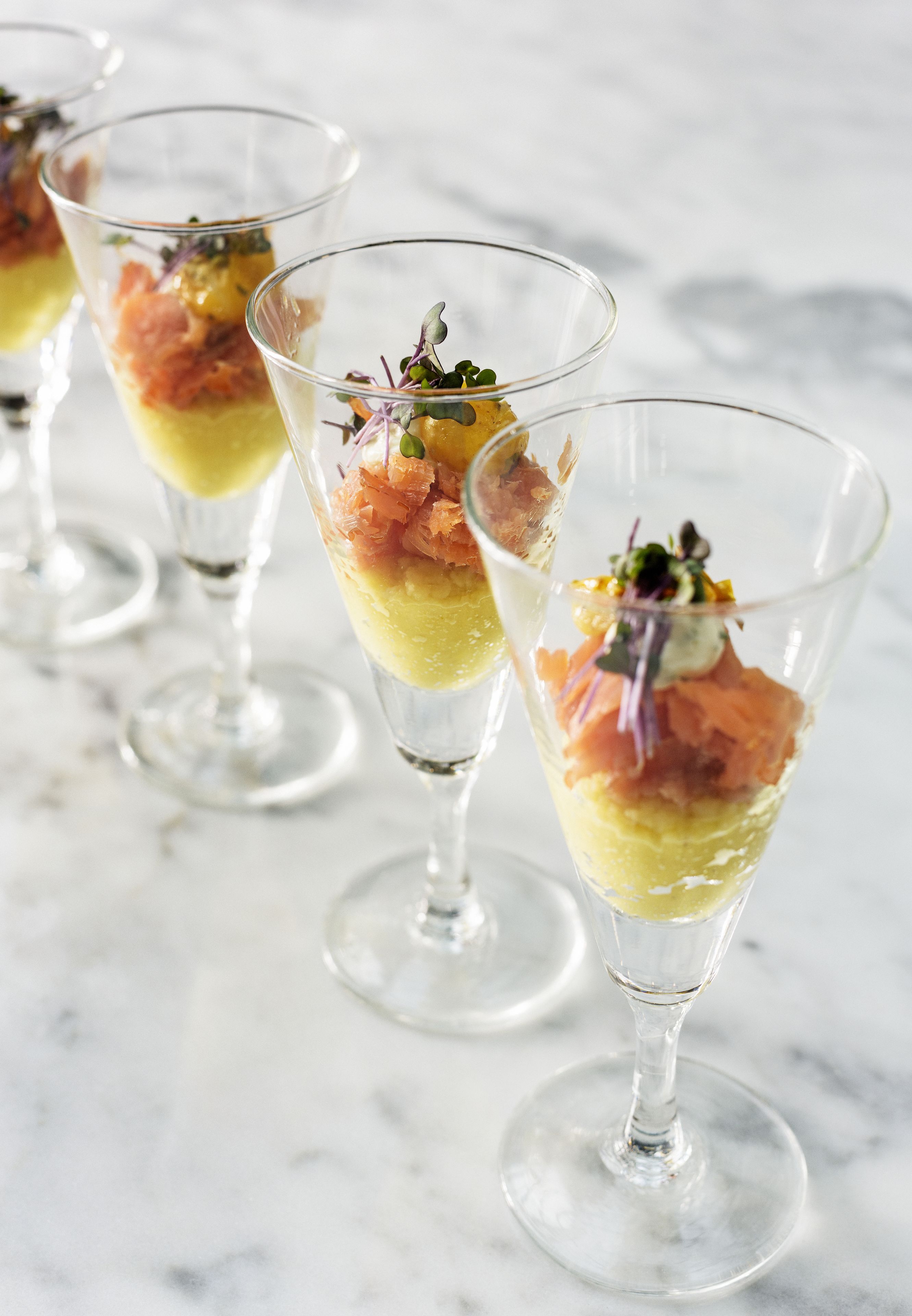 Three dessert glasses with layered fillings and garnishes on a marble surface.